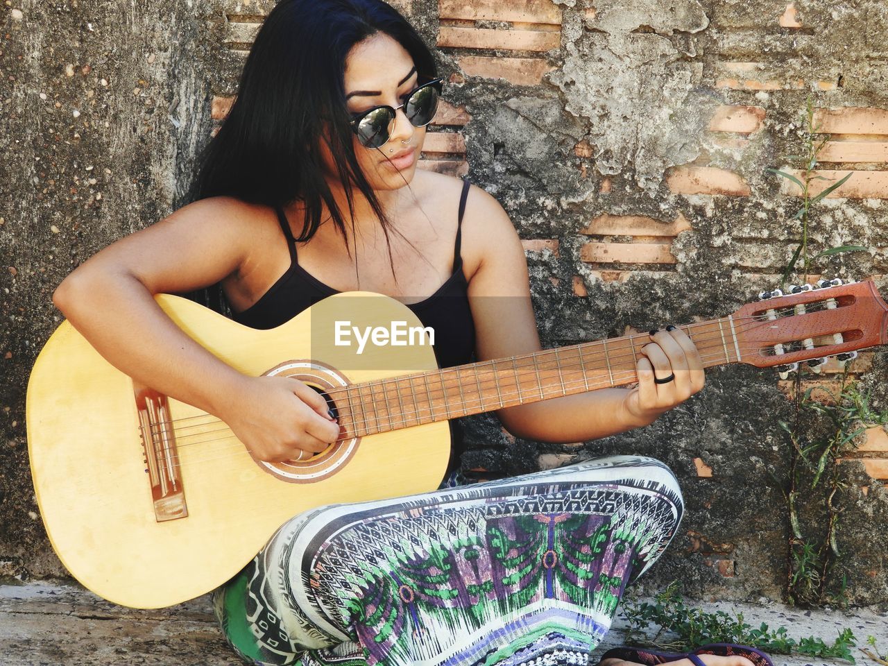 Young woman playing guitar while sitting by old wall