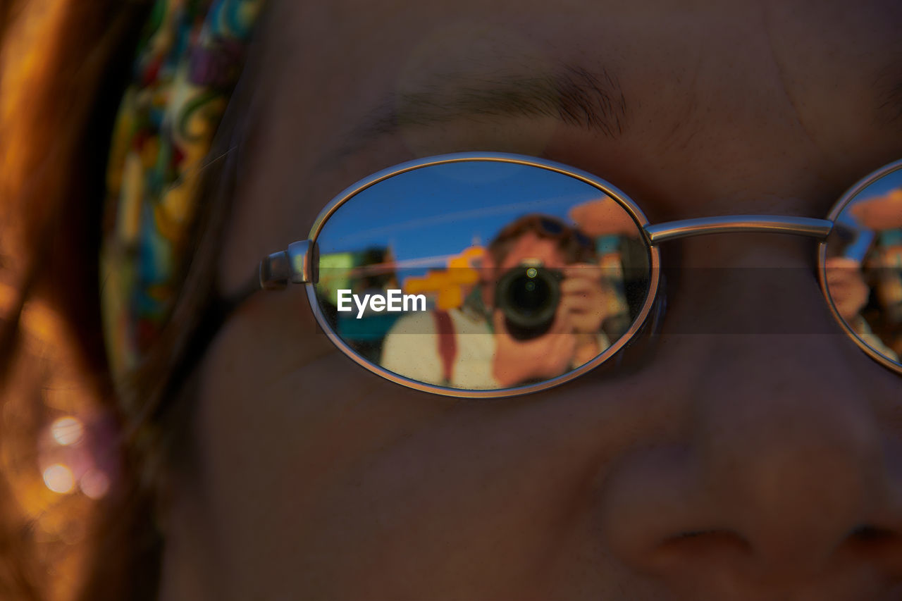 Close-up portrait of young woman with reflection of man in sunglasses