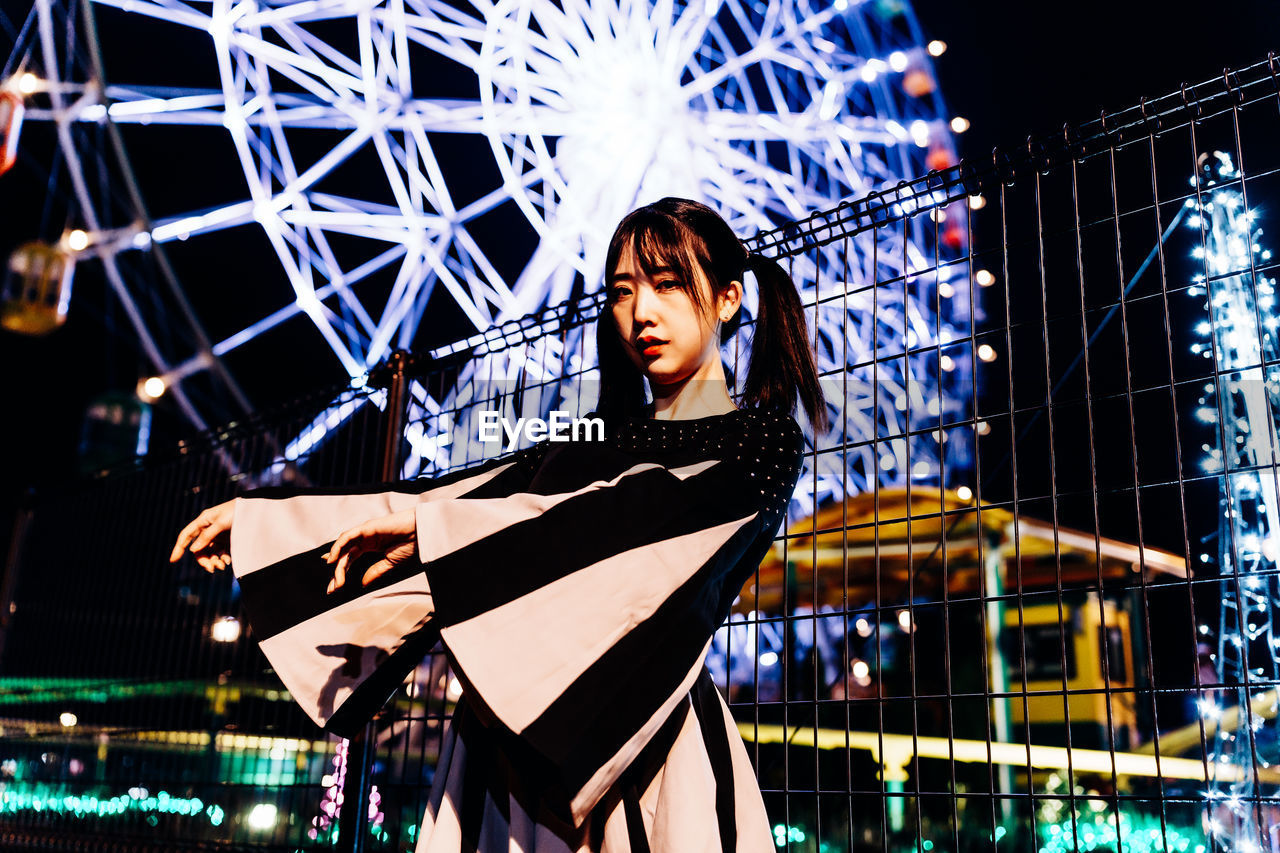 one person, night, performance, amusement park, illuminated, stage, arts culture and entertainment, adult, amusement park ride, women, musical theatre, young adult, emotion, architecture, happiness, clothing, portrait, built structure, person, lifestyles, standing, looking, outdoors, positive emotion, city, female, low angle view, smiling