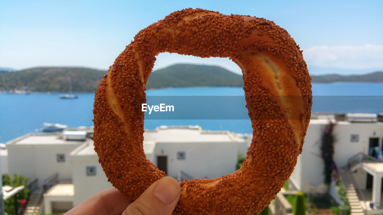 Close-up of person holding pretzel against sea