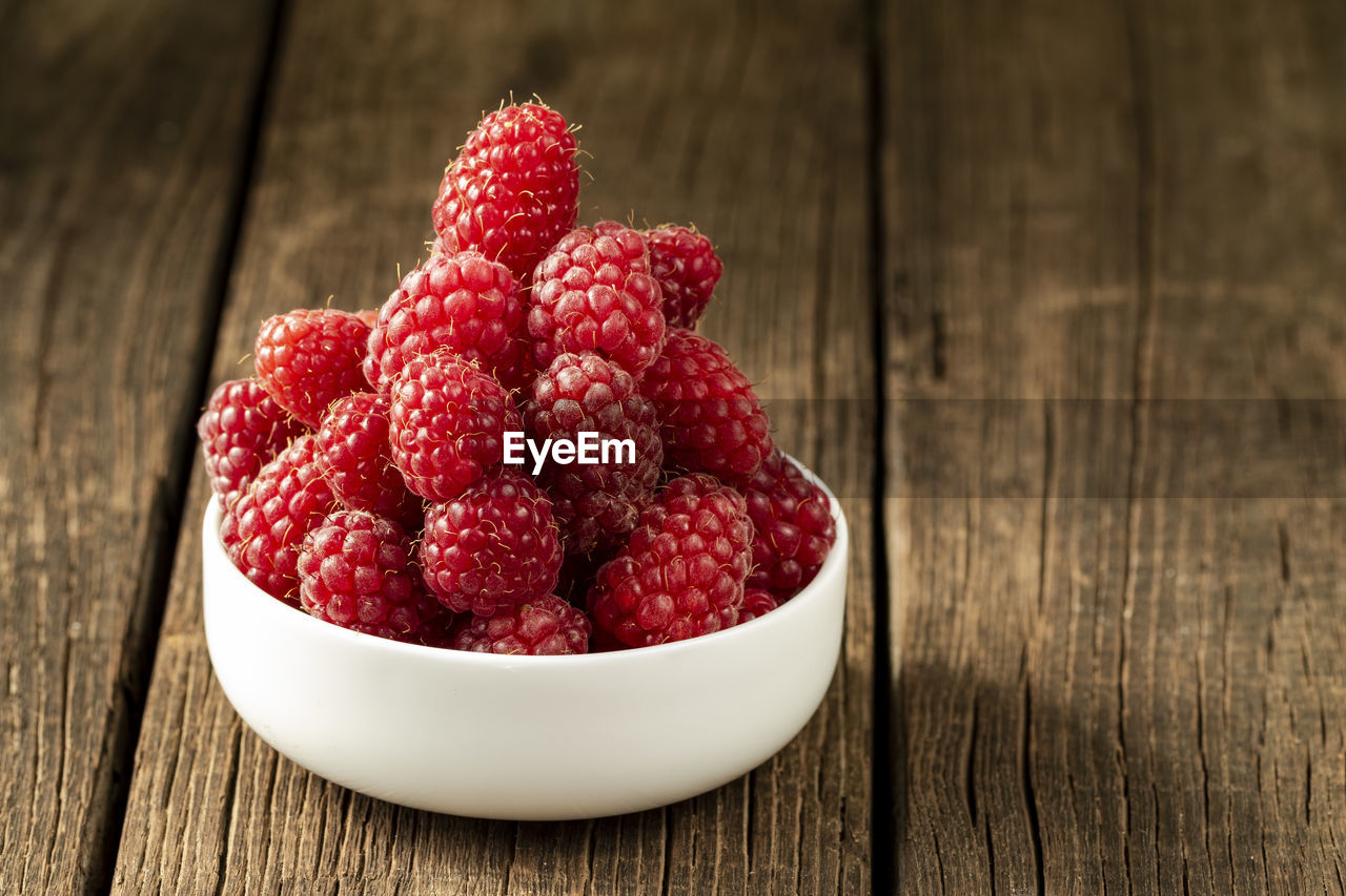 Fresh ripe raspberries in a white ceramic bowl on a dark brown wooden table with space for text