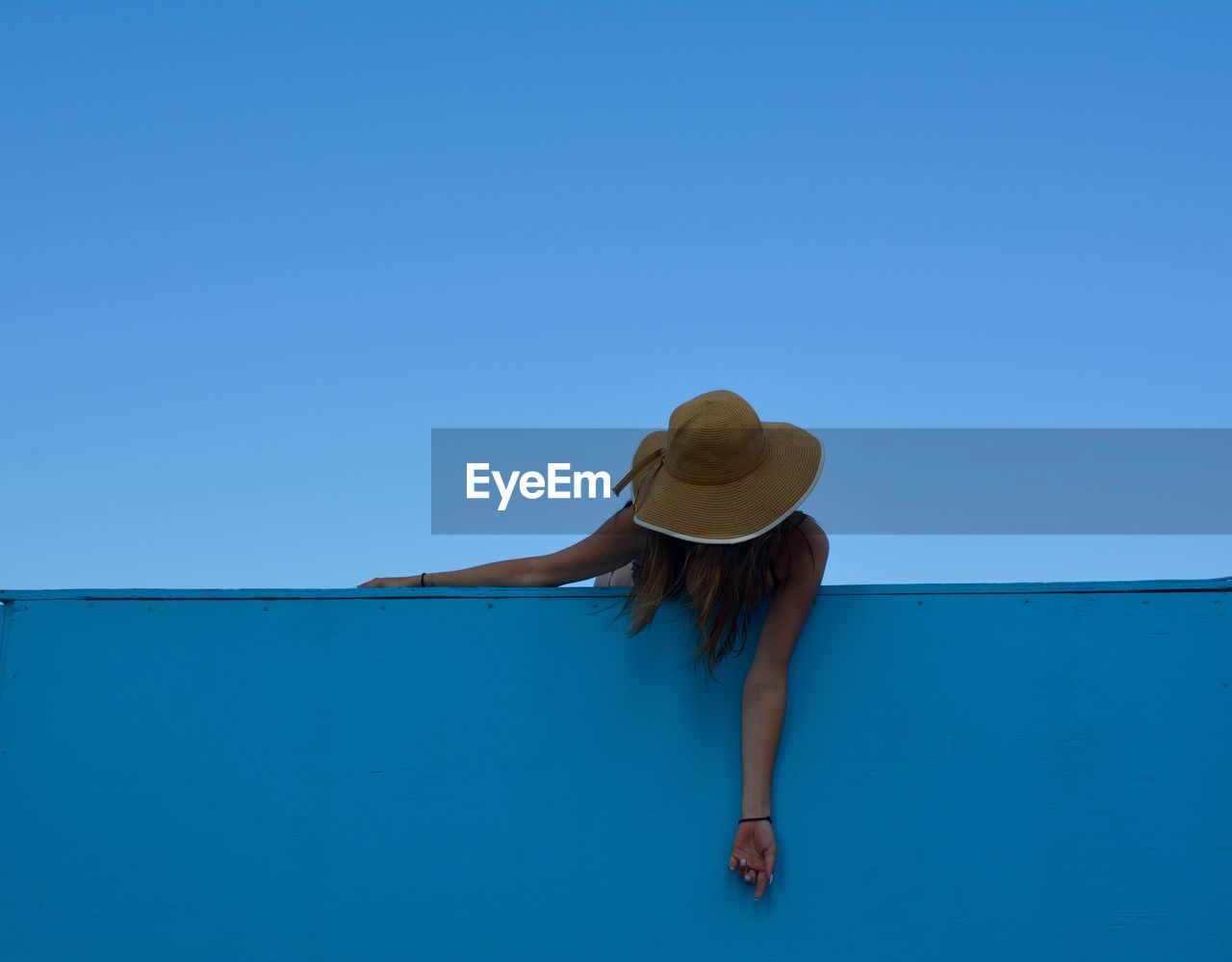 Woman wearing hat by wall against clear blue sky