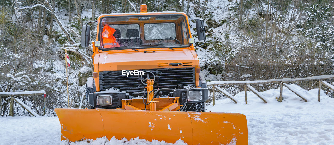 snow, cold temperature, winter, snowplow, snow removal, transportation, mode of transportation, nature, vehicle, tree, orange color, land vehicle, plant, snow blower, day, land, snowing, no people, outdoors, motor vehicle, yellow, off-roading, white, forest, environment, landscape