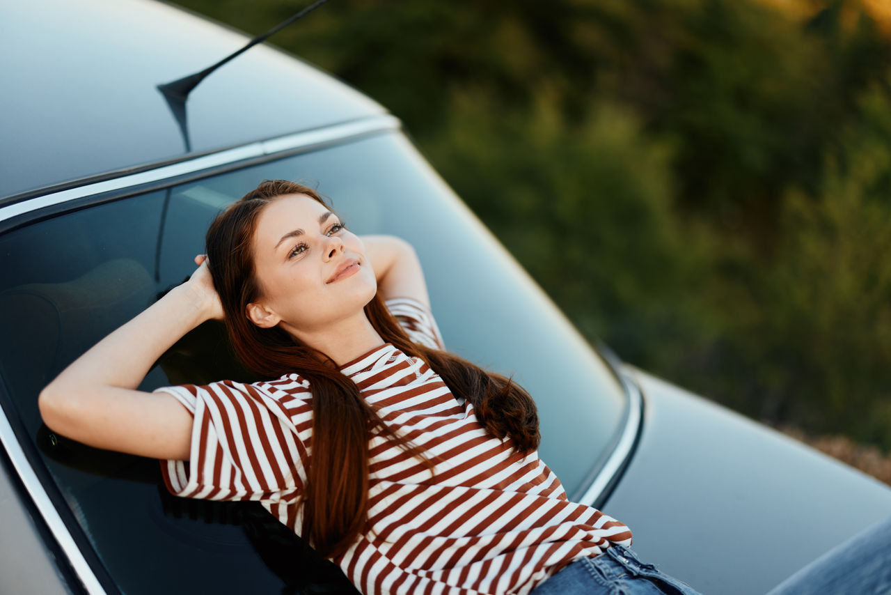 portrait of smiling young woman sitting on car