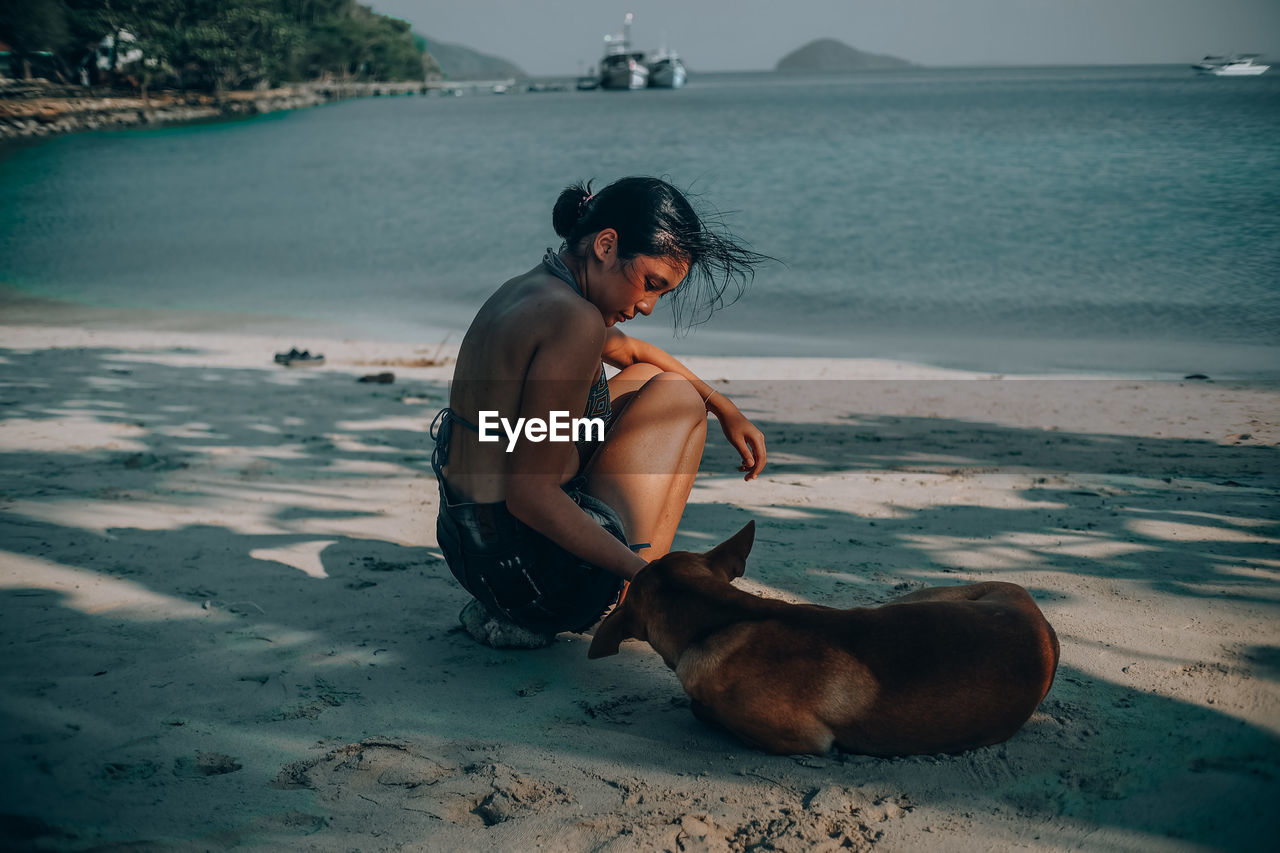 Side view of woman playing with dog at beach