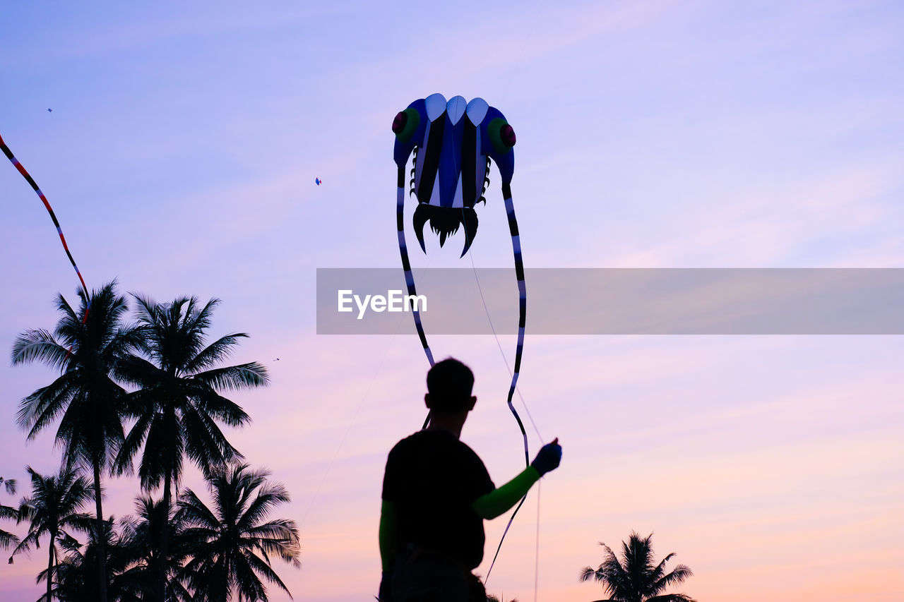 Silhouette man flying kite against sky at sunset