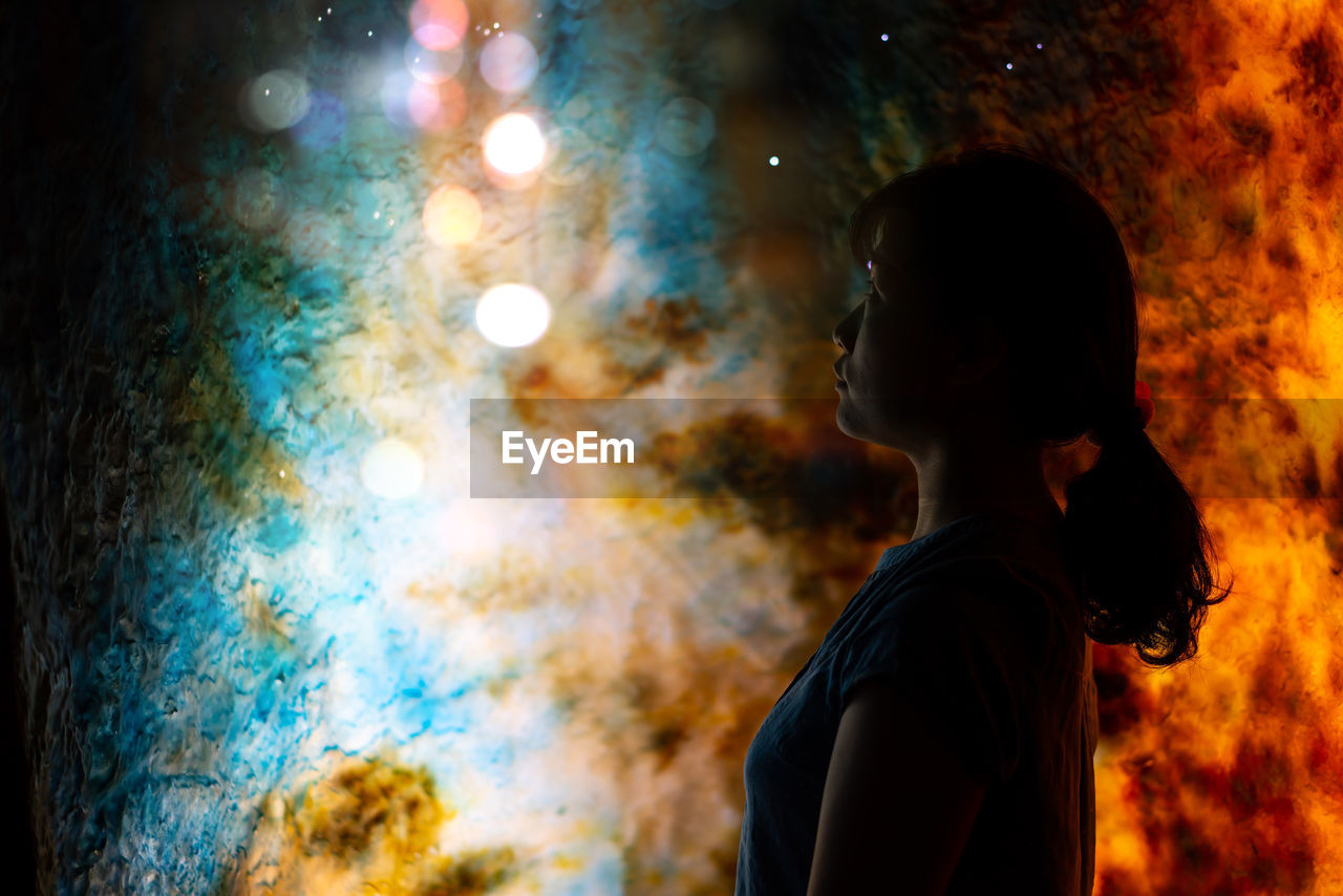 Side view of woman looking at illuminated lights during night