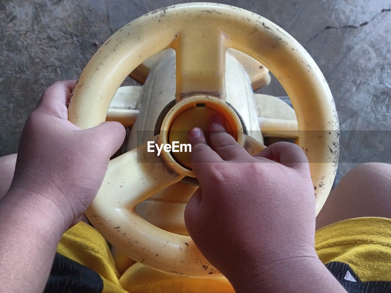 Small child's hand pressing the horn of a yellow toy car