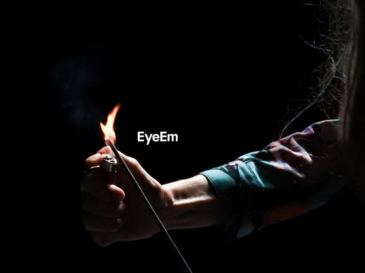 Cropped hand of woman burning incense stick in darkroom