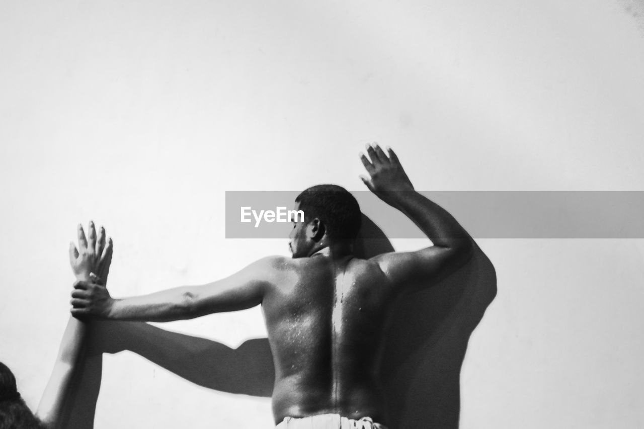 low angle view of shirtless man with arms raised against white background