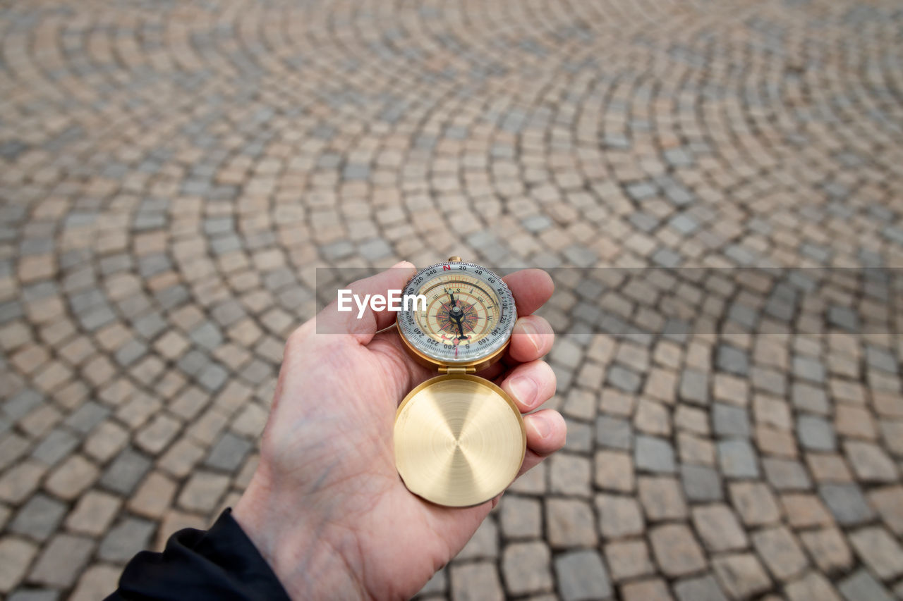 Close-up of hand holding navigational compass on footpath