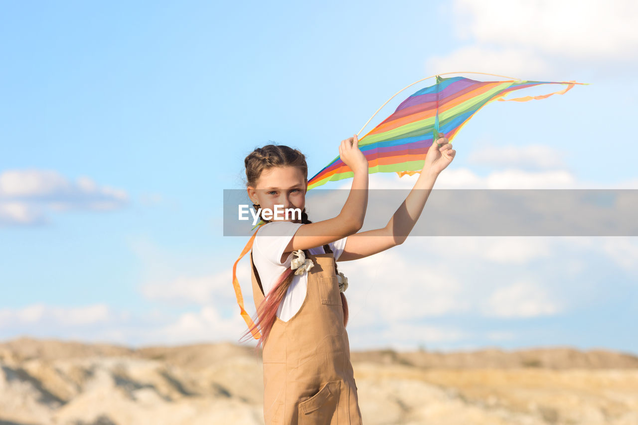 A girl in summer dress launches a kite into the sky in the wild.