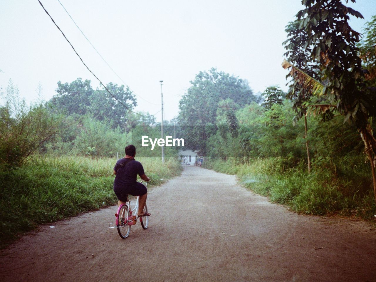 REAR VIEW OF WOMAN RIDING BICYCLE ON ROAD