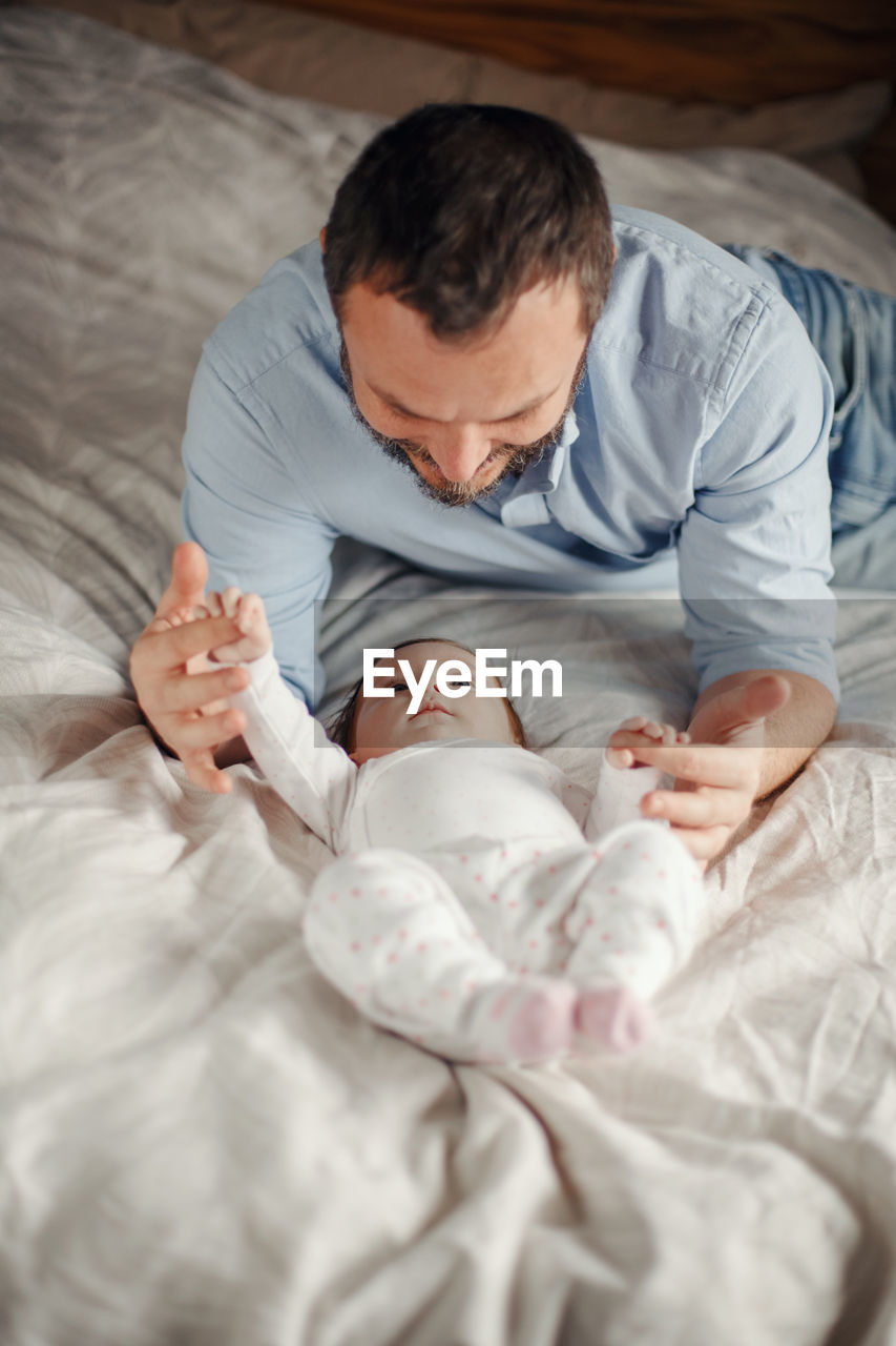 Father playing with toddler daughter on bed at home