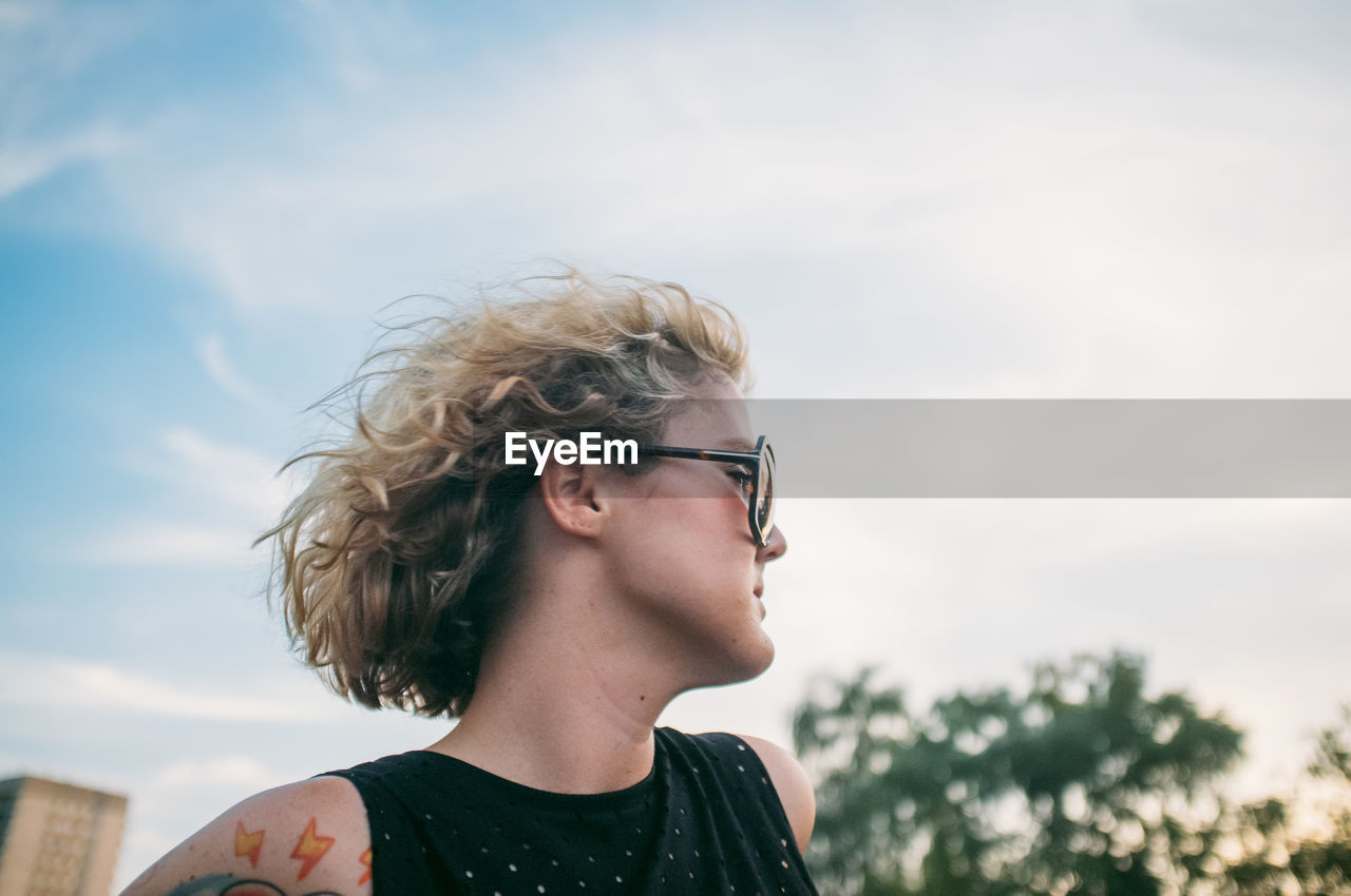 Mid adult woman wearing sunglasses while looking away against sky at sunset