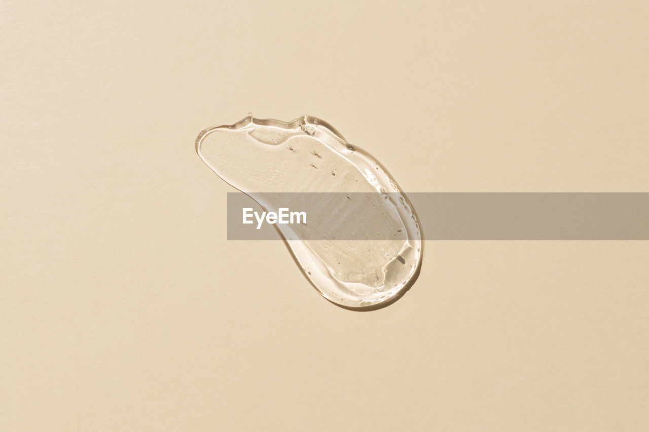 Squeezed cosmetic clear cream gel texture iisolated on beige background. close up transparent serum 