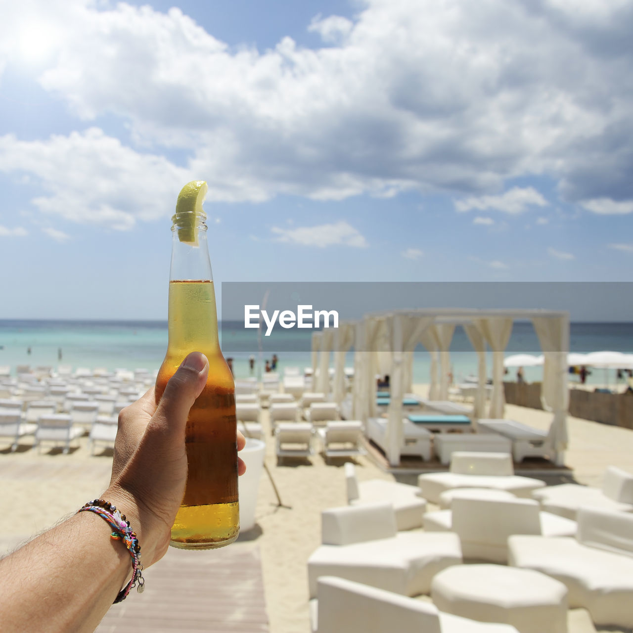 MIDSECTION OF WOMAN HOLDING DRINK AT BEACH