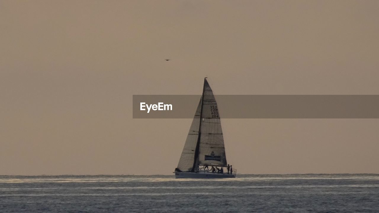 BOAT SAILING ON SEA AGAINST CLEAR SKY DURING SUNSET