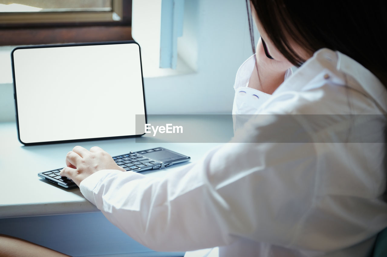 MIDSECTION OF WOMAN USING MOBILE PHONE IN LAPTOP