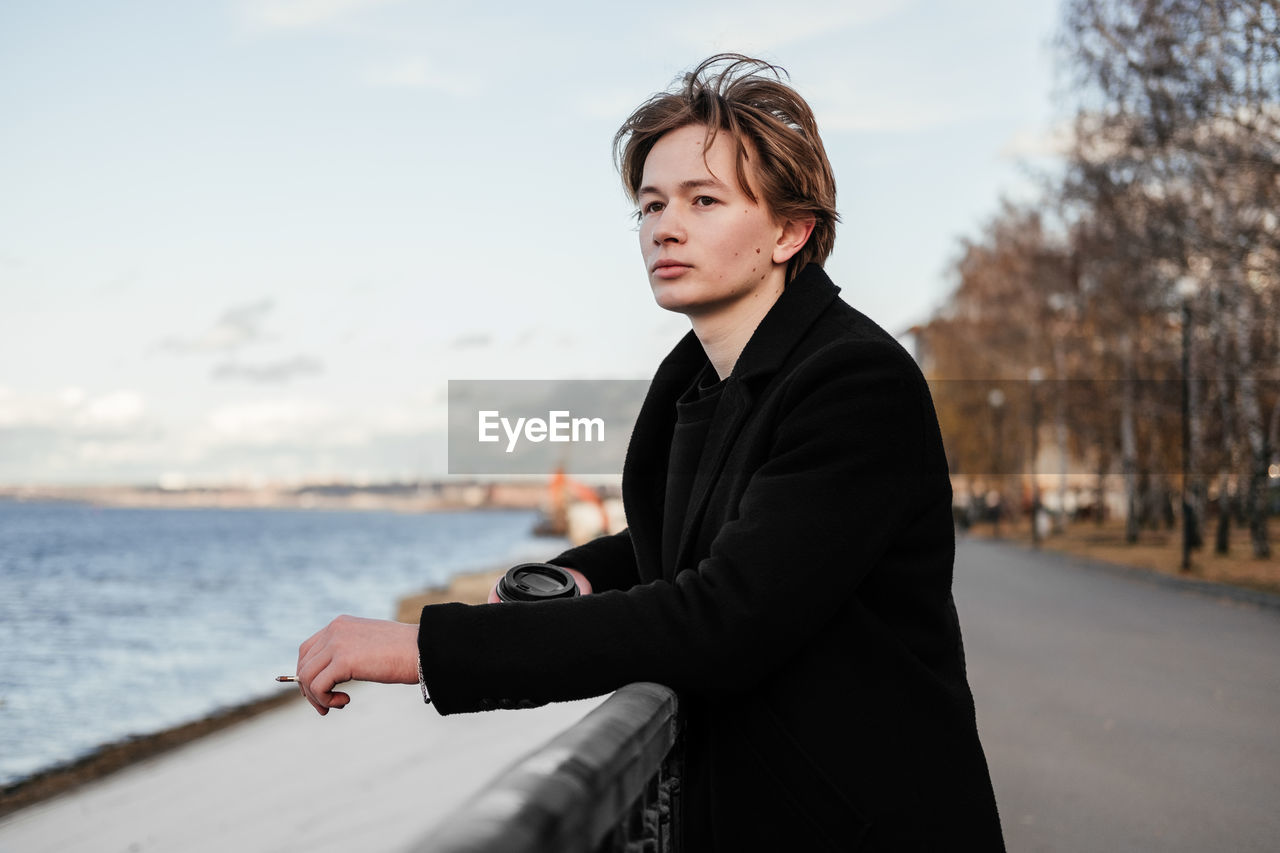 Young man looking away while holding cigarette 