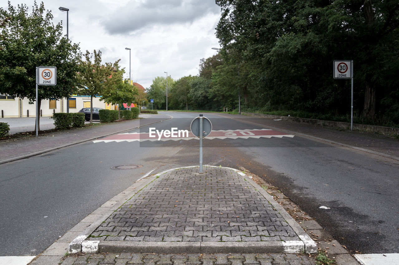 Road signs on sidewalk amidst trees