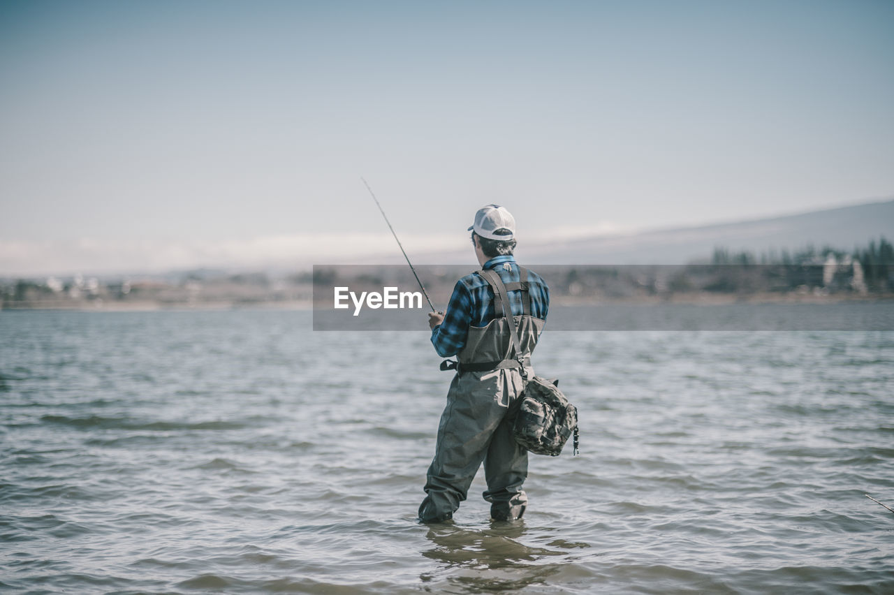 Rear view of man fishing in sea against clear sky