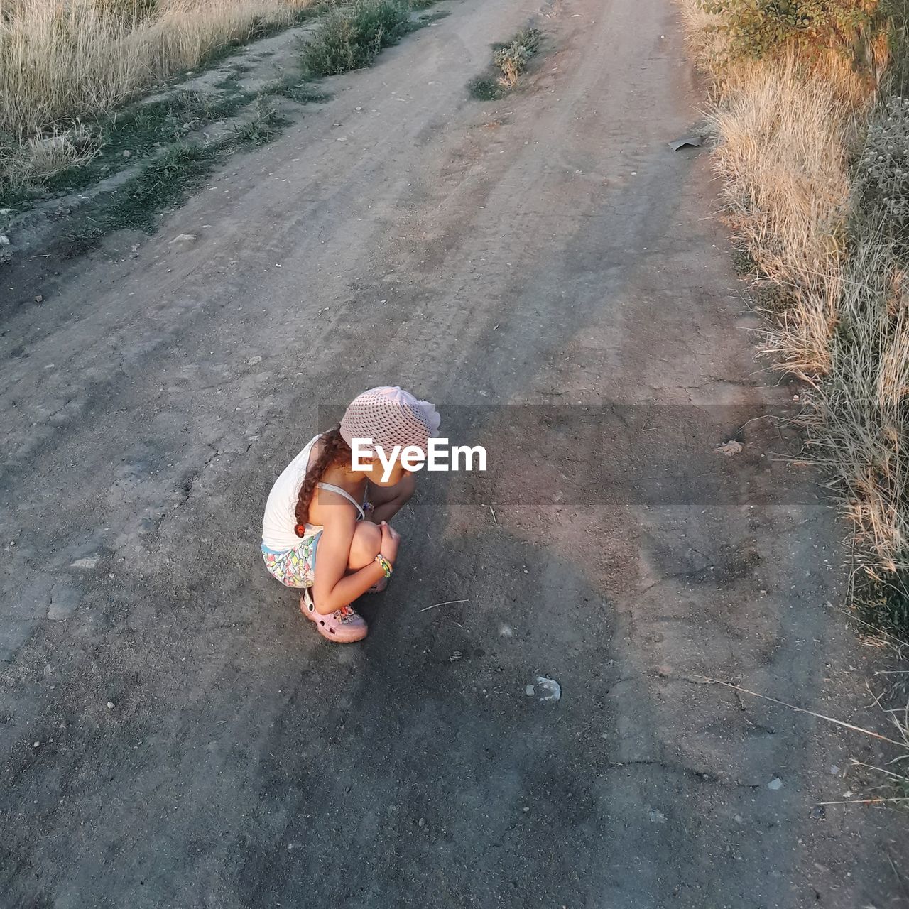 High angle view of girl sitting in hat on road. 