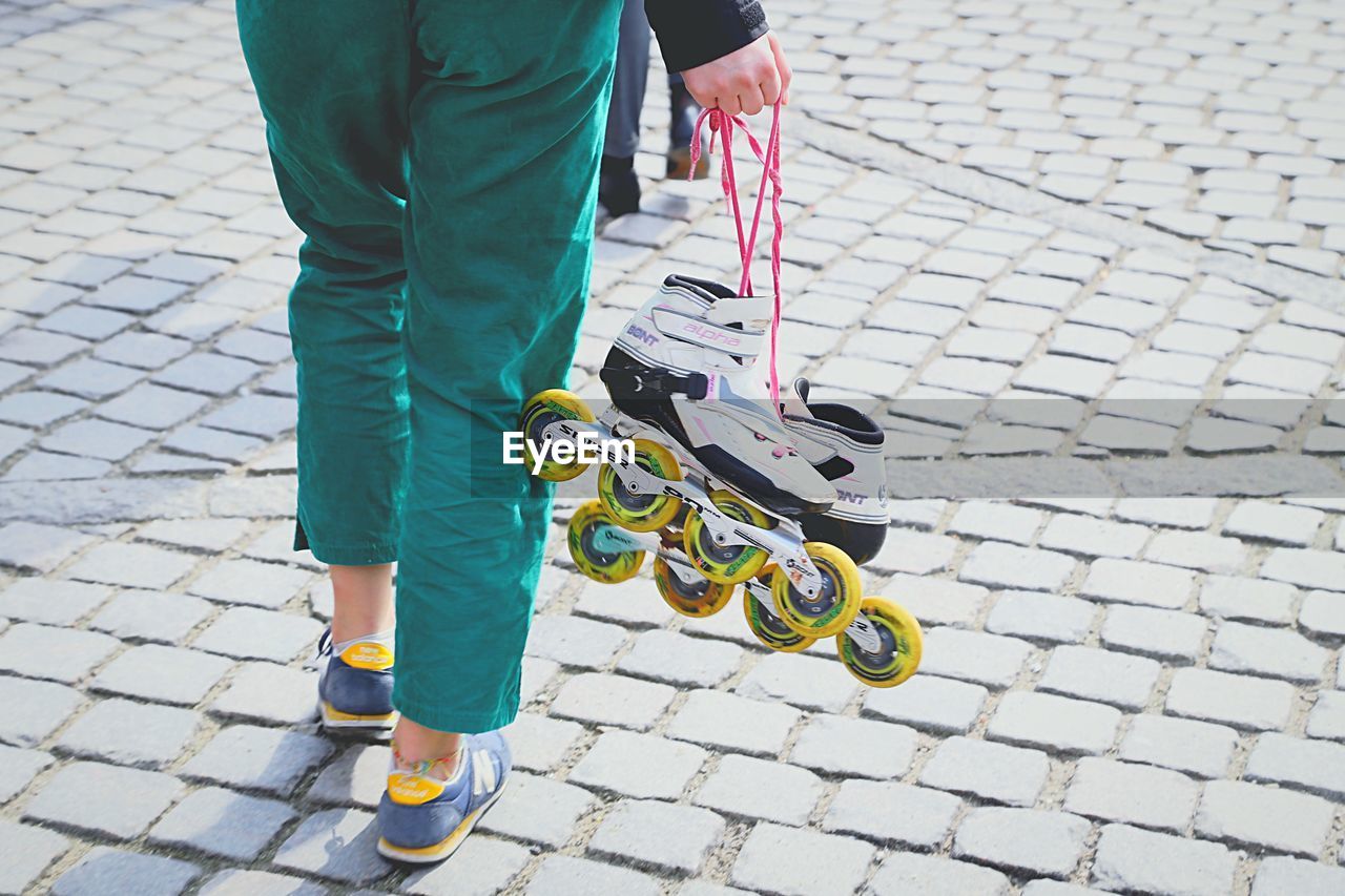 Low section of woman holding skates while standing on footpath