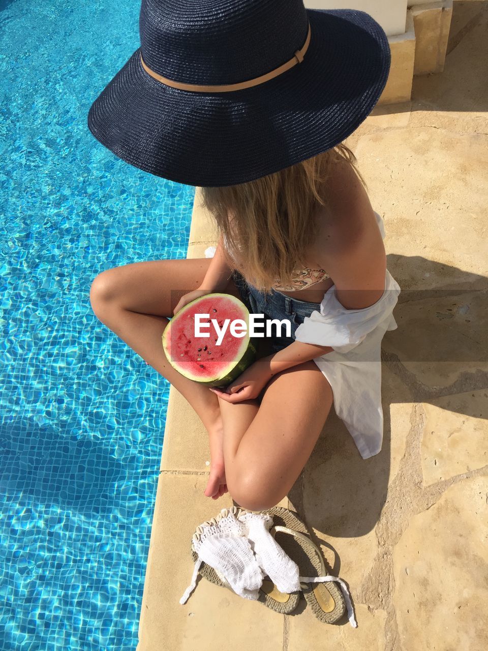 High angle view of woman with hat sitting by swimming pool