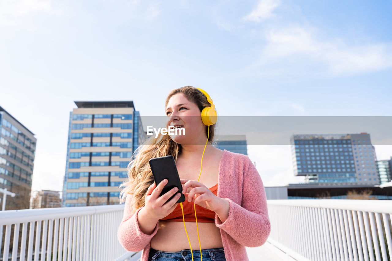 Young woman listening music against sky