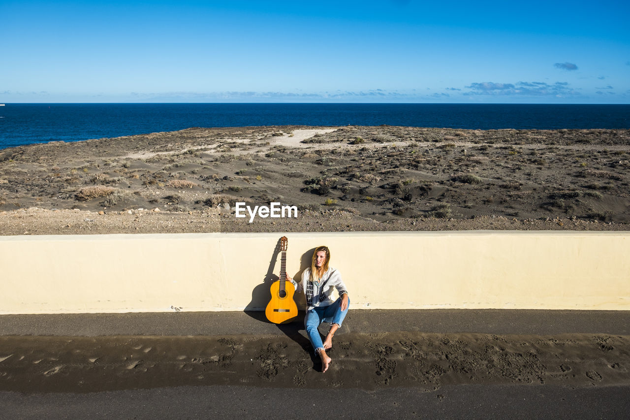 Full length of young woman with guitar sitting at beach