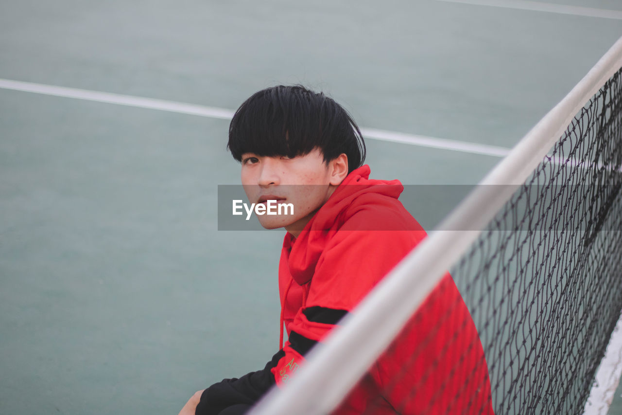 Portrait of man sitting by net on court