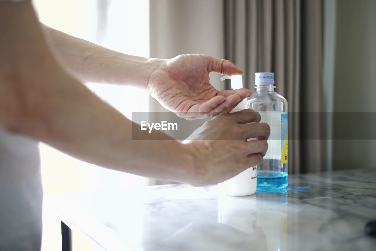 CLOSE-UP OF HAND HOLDING GLASS BOTTLE WITH REFLECTION