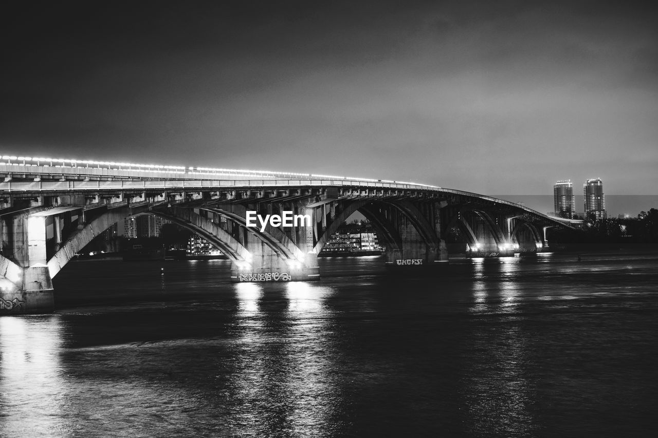 Bridge over river in city against sky at night