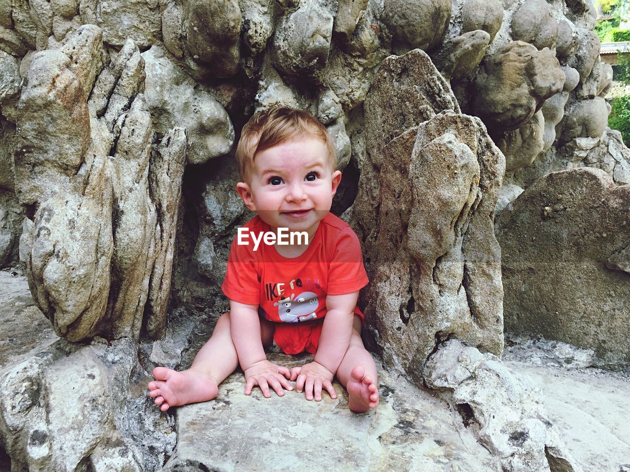 Happy baby boy looking up while sitting by rocks