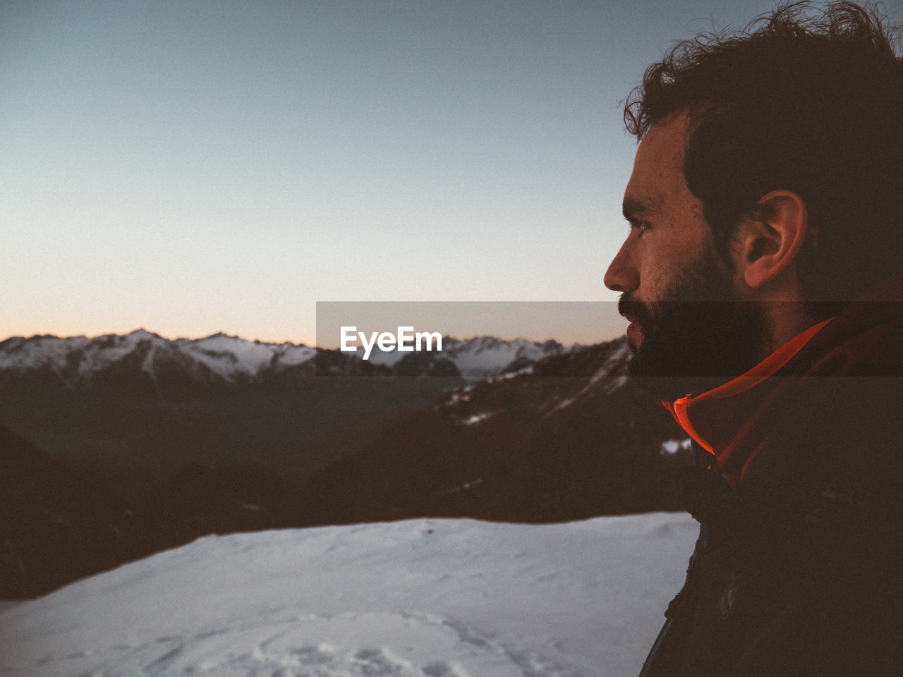 Side view of man looking at snowcapped mountains during sunset