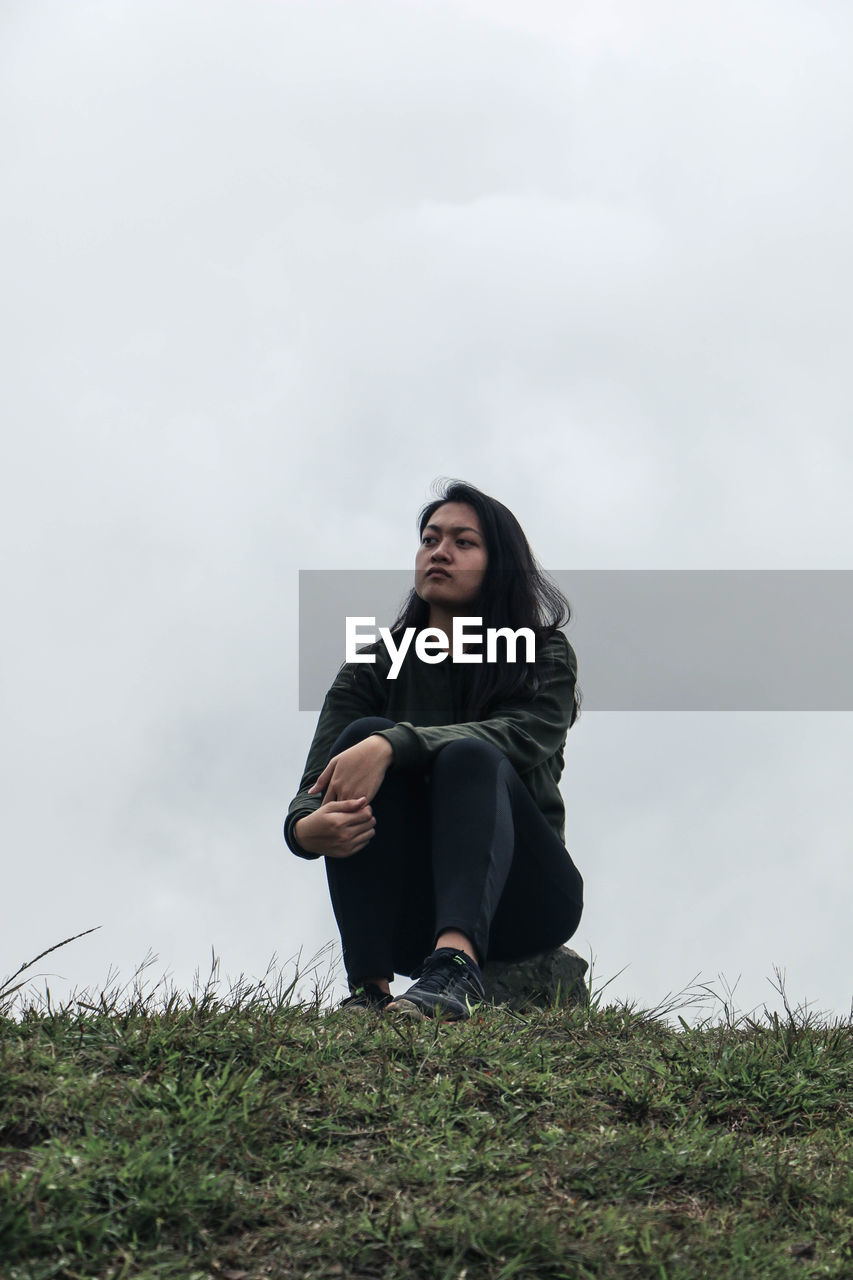 YOUNG WOMAN SITTING ON FIELD