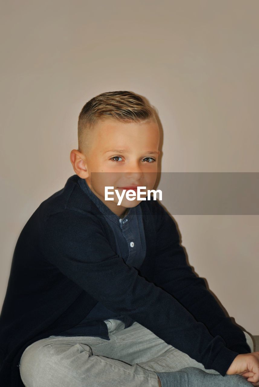 Portrait of boy sitting against gray background