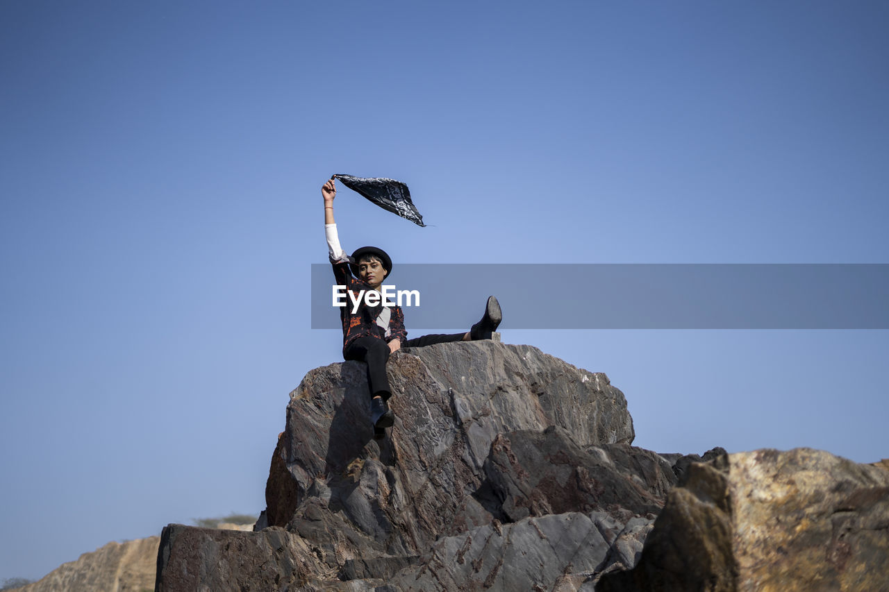 Young beautiful girl sitting on rock in the mountains with holding a hanky on her hand.