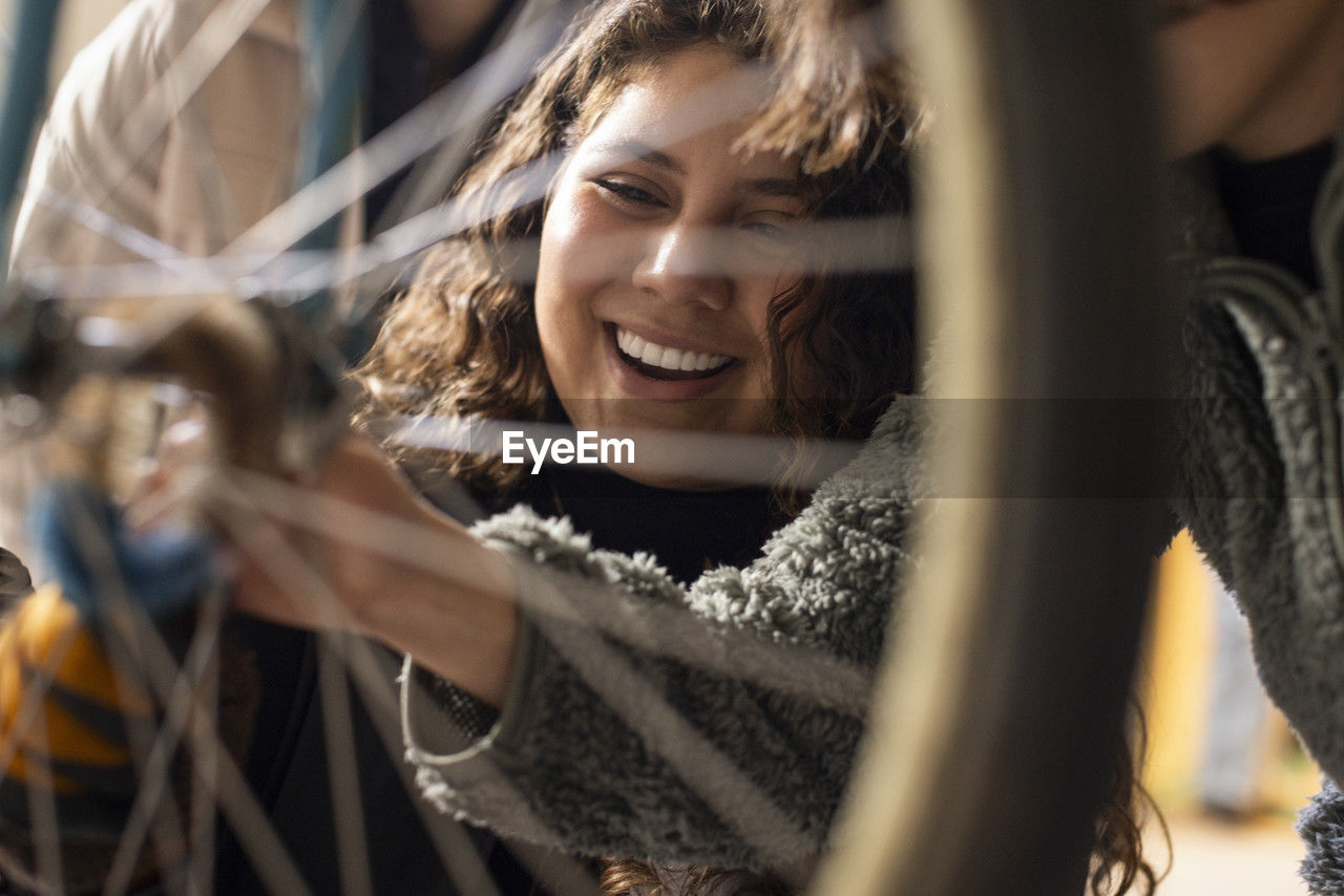 Happy female technician seen through bicycle wheel spokes at recycling center