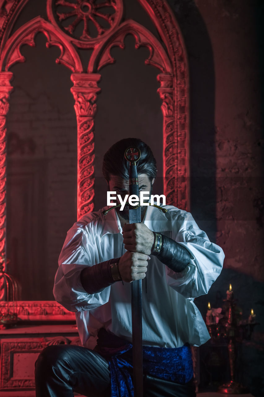 Portrait of man in costume holding sword at abandoned building during night