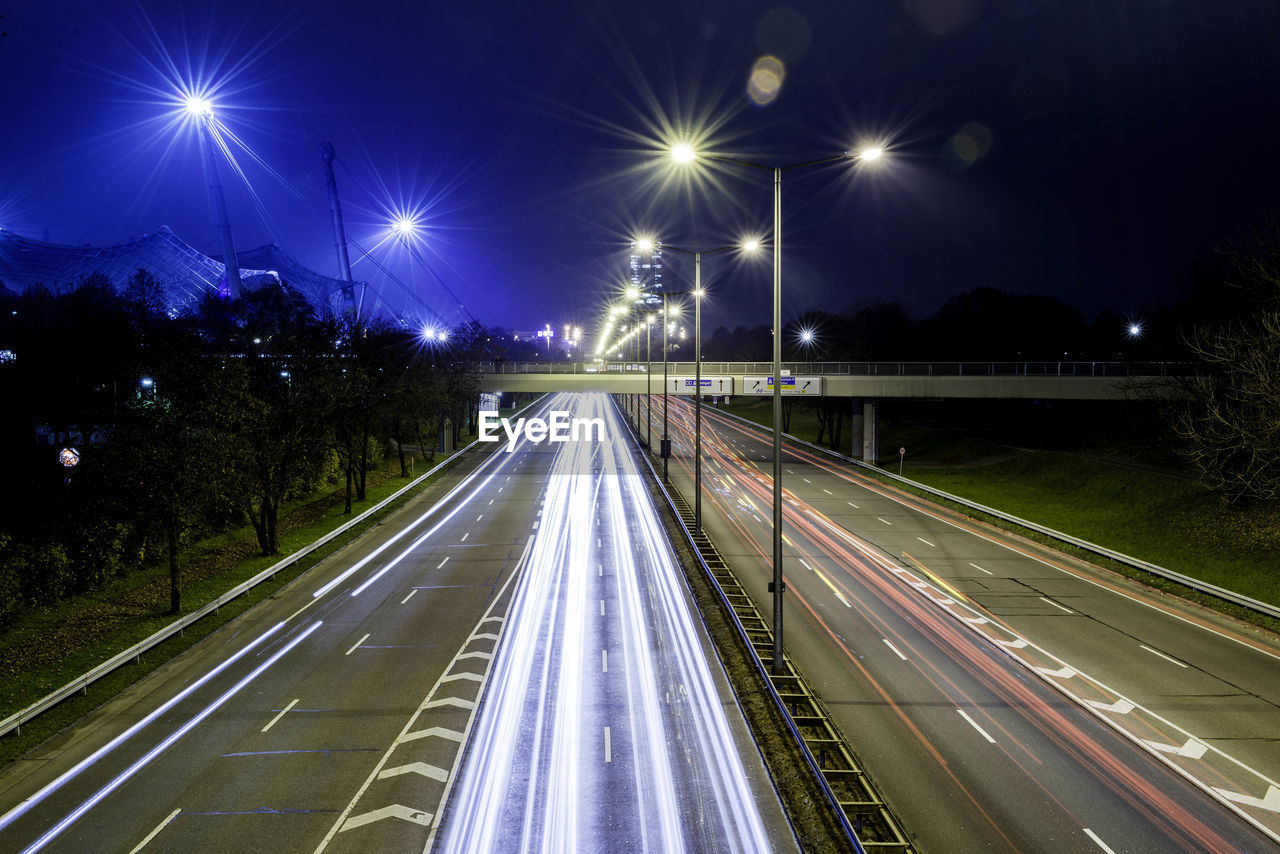 Light trails on illuminated city against sky at night