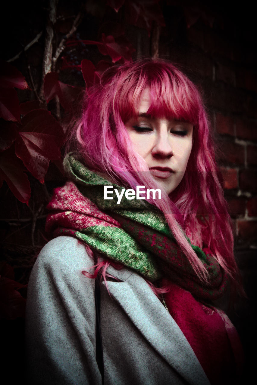 Thoughtful redhead woman standing against brick wall