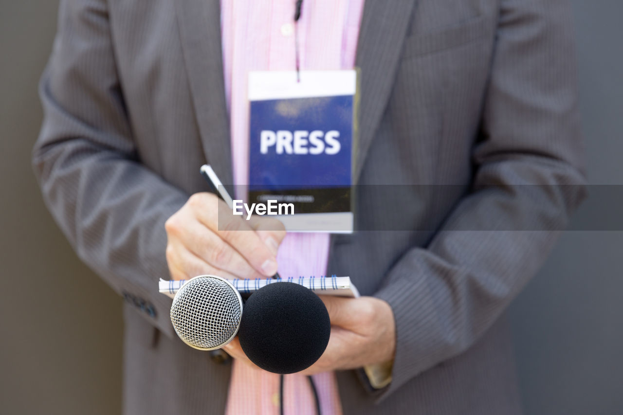 MIDSECTION OF MAN HOLDING CAMERA WHILE STANDING ON MOBILE PHONE