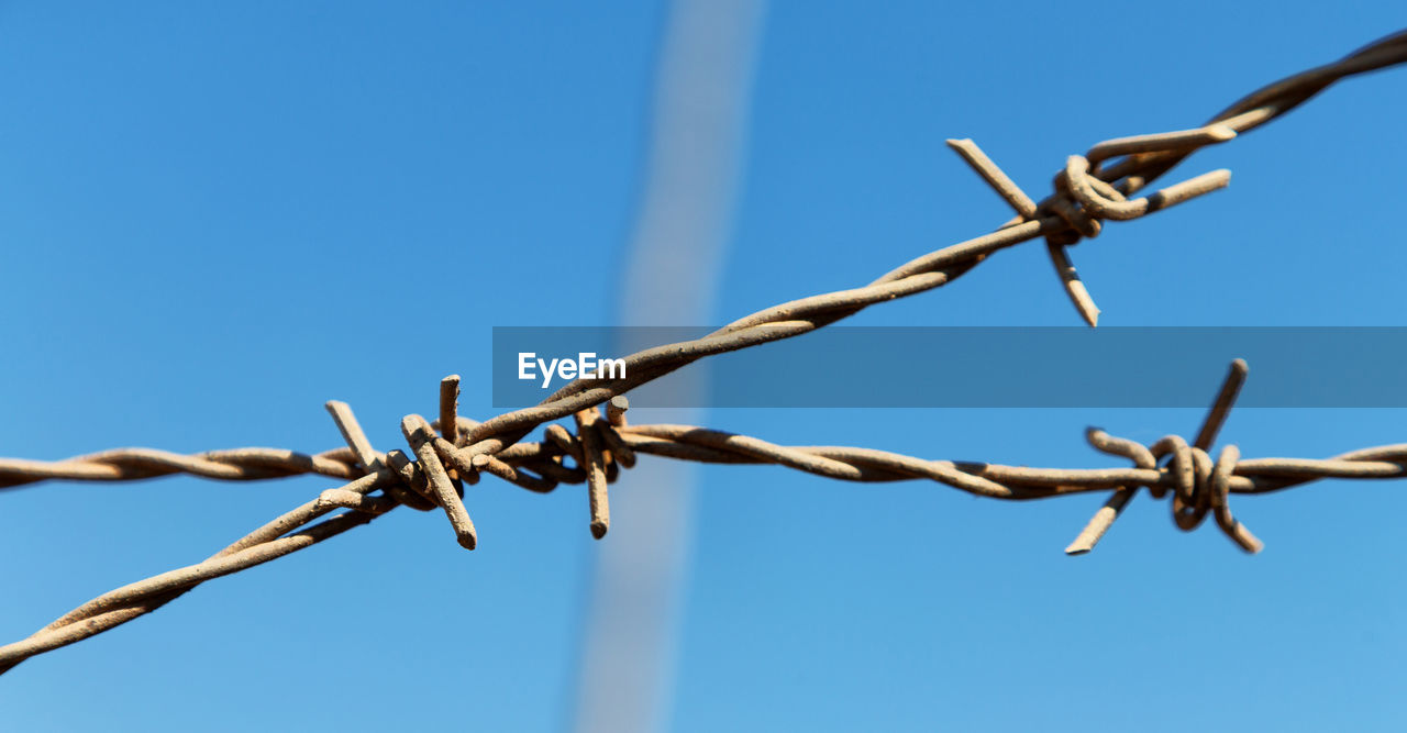 CLOSE-UP OF BARBED WIRE AGAINST CLEAR SKY