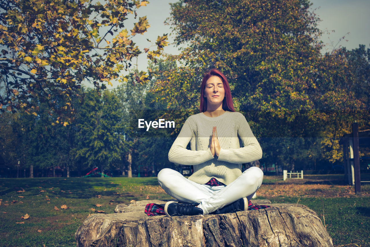 Young woman meditating while sitting on tree stump at park