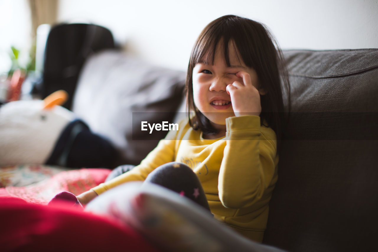 Portrait of cute girl winking eye while sitting on sofa at home