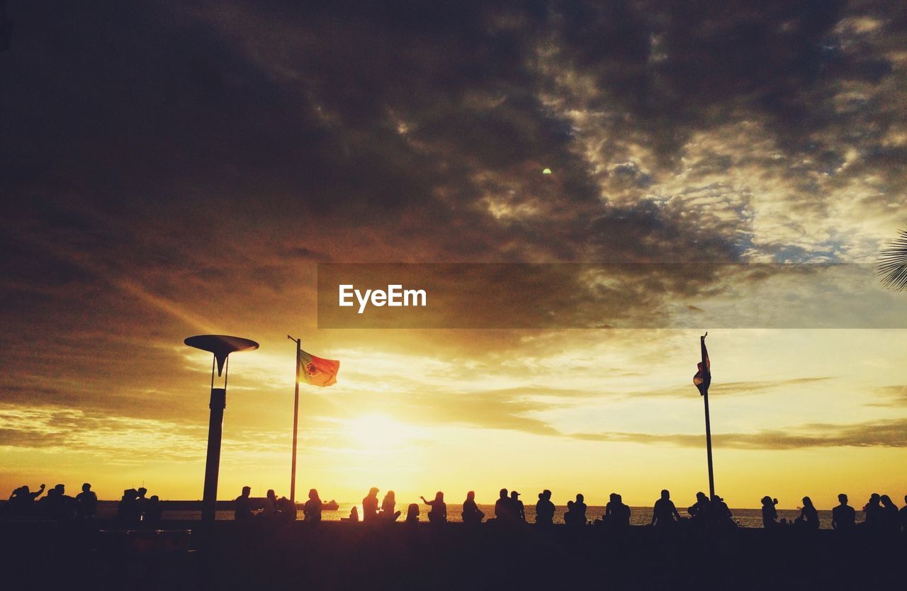 Silhouette people at promenade against cloudy sky during sunset