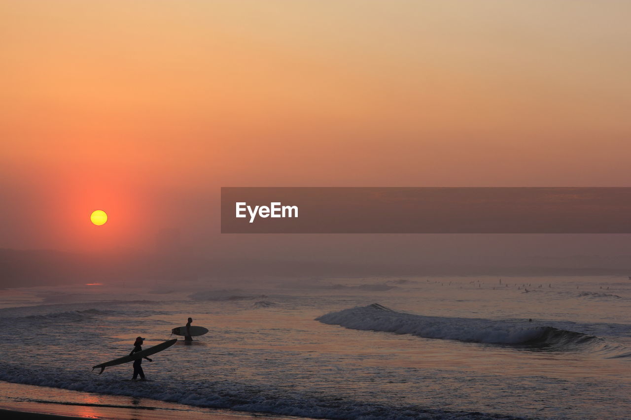 Silhouette men in sea against sky during sunrise