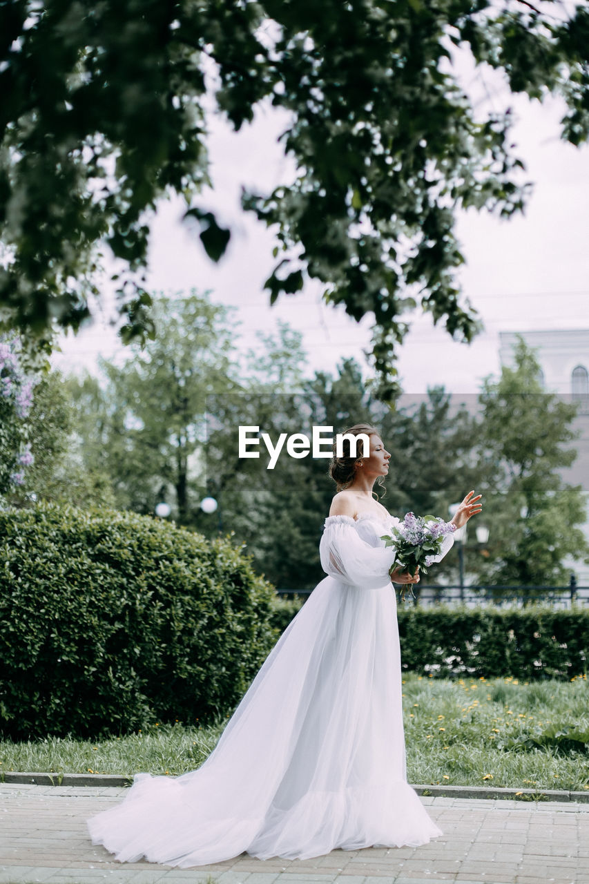 Beautiful bride in a wedding dress walks in a blooming apple-tree park in spring